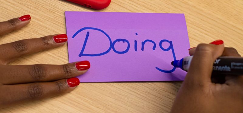 Person writing 'Doing' on a purple Post-it note