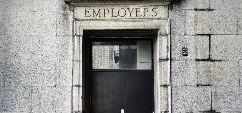 Photo of black wooden door in stone wall with employees craved into the lintal above door